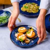 A person is serving small tarts and pasta on blue plates. Voir les images du produit