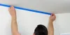 A person is applying blue painter's tape to a wall near the ceiling. Anteprima dell’immagine prodotto