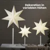 Three illuminated paper star lanterns of varying sizes stand on white pedestals against a dark wooden wall. Podgląd zdjęcia produktu