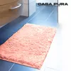 A fluffy pink bath mat is placed on a blue tiled floor next to a wooden cabinet. Náhled obrázku produktu