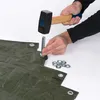 A person is using a hammer to attach an eyelet to a green tarp. Produktbild-Vorschau