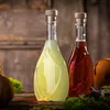 Two glass bottles filled with liquids, one yellow and one red, are placed on a wooden surface with moss and a decorative object in the background. Anteprima dell’immagine prodotto