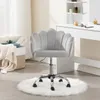 A light gray velvet chair with a petal-shaped backrest is placed on a white fluffy rug in a room with a dressing table in the background. Produktbild-Vorschau