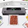 A vacuum sealer machine is shown sealing a bag of sausages on a white countertop, with some fruits and other packaged food items visible in the background. Náhľad obrázku produktu