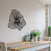 A wall clock shaped like a flower is mounted on a wall above a wooden dining table. Produktbild-Vorschau