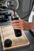 A person is pouring coffee into a black thermos mug on a wooden cutting board. Podgląd zdjęcia produktu