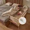A mother is lying in bed next to a baby in a co-sleeper bassinet. The bassinet is attached to the side of the bed. Voir les images du produit