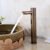 A close-up shot of a vintage-style automatic sensor faucet dispensing water into a decorative ceramic sink. The background features marble-patterned tiles. Podgląd zdjęcia produktu