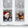 A young boy wearing a Santa hat looks out a frosted window decorated with snowflake stickers, with a fireplace visible in the background. Produktbild-Vorschau