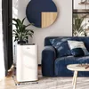 A white portable air conditioner is placed next to a blue sofa in a living room. Produktbild-Vorschau