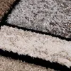 A close-up view of a textured rug with geometric patterns in shades of beige, gray, and brown, separated by black lines. Produktbild-Vorschau
