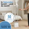 A person is standing next to a garment steamer in a bedroom setting, with a bed and closet visible. Náhled obrázku produktu