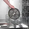A hand is placing a circular metal rack with holes into a dishwasher rack. Produktbild-Vorschau
