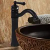 A black faucet is shown above a decorative brown sink, with a folded towel in the background. Náhled obrázku produktu