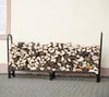 A black metal firewood rack filled with chopped wood, placed on a paved patio in front of a cream-colored building. Náhľad obrázku produktu