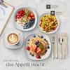 A flat lay of breakfast items including a fruit salad, yogurt with granola and berries, pancakes with fruit and nuts, and a cup of coffee, arranged on a marble-like surface. Produktbild-Vorschau
