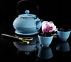 A blue cast iron teapot set with two cups and a tea scoop, arranged on a reflective black surface with a pink orchid. Náhled obrázku produktu
