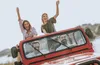 Four young people are riding in a red jeep, with two women in the back waving and smiling, and two men in the front. Anteprima dell’immagine prodotto