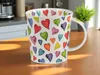 A mug with a heart pattern sits on a wooden table. Produktbild-Vorschau