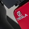A close-up shot of a red vehicle's emblem and part of its body. Produktbild-Vorschau