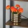 A gold vase with orange flowers on a shelf. Náhled obrázku produktu