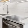 A close-up view of a kitchen countertop with a sink, faucet, and a stainless steel cutting board. Produktbild-Vorschau
