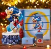 A Sonic the Hedgehog themed advent calendar or display box with a Sonic figure on a skateboard, set against a festive, bokeh background with Christmas lights. Podgląd zdjęcia produktu