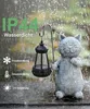 A cat garden statue holding a lantern in the rain, with text overlays indicating product features. Produktbild-Vorschau