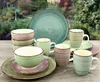 A collection of stoneware dishes and mugs arranged on a wooden table with a garden in the background. Produktbild-Vorschau