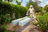 A woman watering plants in a garden with two plant tunnels. Produktbild-Vorschau