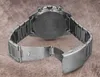 The back of a silver metal watch with an open clasp is shown on a textured brown surface. Voir les images du produit
