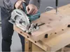 A person is using a circular saw to cut a piece of wood on a workbench. Produktbild-Vorschau