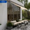 An outdoor seating area of a cafe or restaurant with tables, chairs, and a sofa, shaded by an awning. Náhľad obrázku produktu