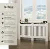 A white radiator cover is shown in front of a window, with decorative items on top. A text overlay describes its features. Náhled obrázku produktu