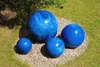 Four blue ceramic spheres of varying sizes are arranged on a bed of gravel in a garden setting. Produktbild-Vorschau