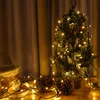 A small decorated Christmas tree with lights, pinecones, and a basket on a wooden surface, with curtains in the background. Náhľad obrázku produktu