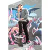 A man stands on a concrete structure in front of a graffiti-covered wall, holding a red object. Náhľad obrázku produktu
