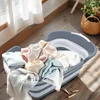 A foldable laundry basket filled with clothes is placed on a wooden floor near a window with sheer curtains. Anteprima dell’immagine prodotto