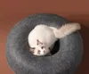 A fluffy white cat with brown markings is lying in a round, dark gray cat bed. Produktbild-Vorschau