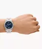 A person's wrist wearing a silver watch with a blue face. Náhled obrázku produktu