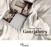 An open magazine lies on a rumpled white bedsheet, with text overlaying the image. Produktbild-Vorschau