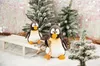 Two plush penguins are sitting in the snow with small, flocked Christmas trees and a sled. Voir les images du produit