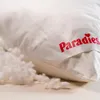 A close-up shot of a white pillow with a red logo and some loose filling spilling out. Produktbild-Vorschau