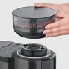Hands holding a coffee bean container above a coffee machine. Produktbild-Vorschau