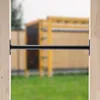 A black metal bar is mounted between two wooden posts, with a blurred playground structure in the background. Produktbild-Vorschau