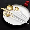 A set of gold and white cutlery laid out on a white plate. Voir les images du produit