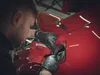 A person wearing black gloves is working on the fuel cap of a red car. Produktbild-Vorschau
