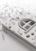 A close-up view of a white and gray plastic component, possibly part of a toy or model, with small clear plastic pellets scattered around it on a white surface. Náhľad obrázku produktu