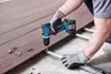 A person wearing work gloves is using a cordless drill to attach a composite decking board to a metal frame. Náhled obrázku produktu