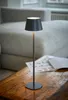 A modern gray table lamp sits on a wooden table in front of a couch. Produktbild-Vorschau